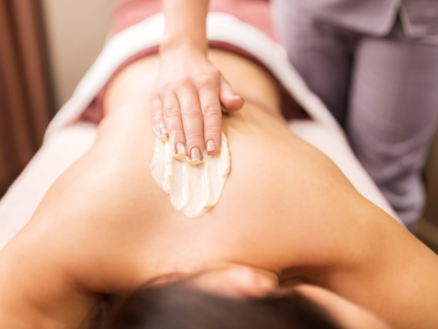 people, beauty, healthy lifestyle and relaxation concept - beautiful young woman lying and having back massage with cream at spa